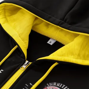 Close-up of mens black zip hoodie with yellow inner hood, metal zipper and chest print.
