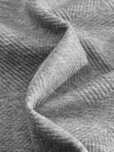 Vue détaillée de la texture du tissu jacquard gris avec des pliures géométriques.