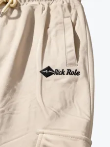 Detailed view of beige mens casual cargo pants with drawstring waist and logo embroidery.