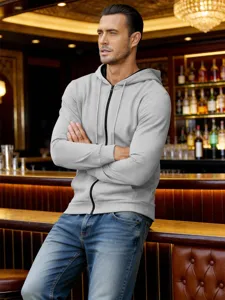 Vue de detail du sweat a capuche gris clair zippe porte par un modele au comptoir.