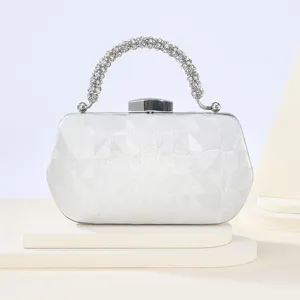 Detalle elegante de bolso de mano plateado con asa de estrás y cierre metálico.