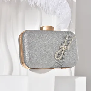 Detail view of silver glitter evening clutch bag with elegant rhinestone bow and gold metal frame.