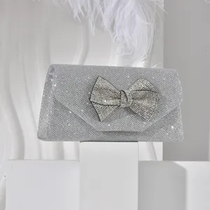 Silver glitter evening clutch bag featuring a dazzling rhinestone bow detail for parties.