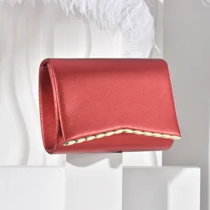 Red evening clutch bag detail showcasing fine textured leather and a sleek gold metallic wave trim.