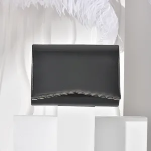 Close-up detail shot of black textured evening clutch featuring decorative metal scalloped edge.