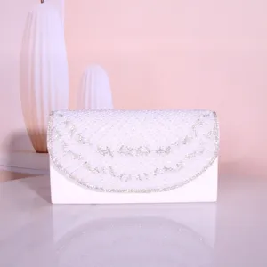 Detail shot of elegant white evening clutch bag featuring intricate pearl and rhinestone decorations.