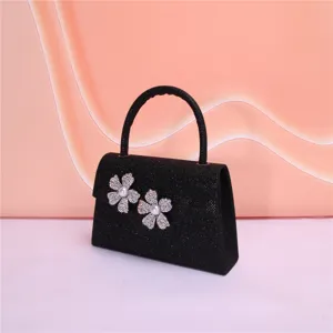 Black glitter evening bag detail showing crystal pearl flower ornaments and single handle.
