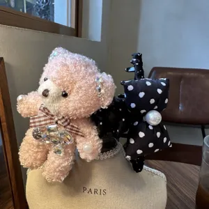Nahaufnahme des flauschigen Bären-Haarclips mit glänzenden Strasssteinen und karierter Schleife.