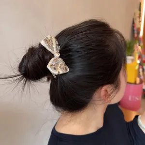 Chic champagne rhinestone bow hair tie detail, sparkling crystal bun holder accessory.
