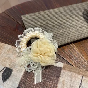 Closeup of a sweet Korean style hair scrunchie with lace trim, beige fabric rose and crystals.