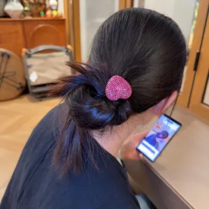 Close-up detail of a sparkling pink rhinestone heart hair tie worn on a ponytail, elegant.