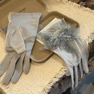 Gros plan de gants en dentelle grise ornés d'un papillon de perles et de pompons.