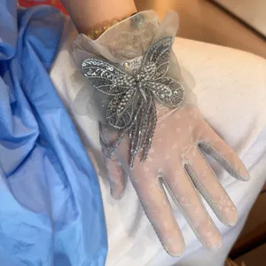 Gros plan de gants courts en dentelle délicate ornés d'un papillon brodé de sequins et de franges fluides.