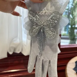 Détail de gant en dentelle argentée avec papillon en sequins et pompons de perles.