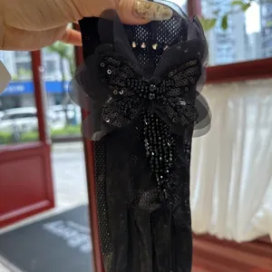 Gros plan de gants en dentelle noire avec papillon en sequins et pendentifs en cristaux brillants.