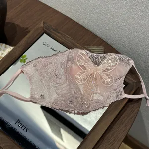Vista dettagliata della maschera antipolvere in pizzo rosa con strass scintillanti e farfalla.