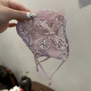 Mascherina in pizzo rosa con paillettes brillanti, bordo in strass e dettaglio di farfalla.