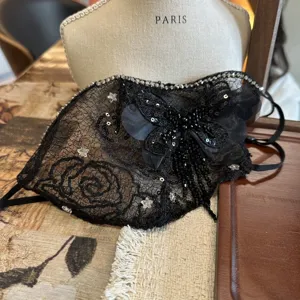 Dettaglio maschera facciale in pizzo nero, farfalla di strass e paillettes.