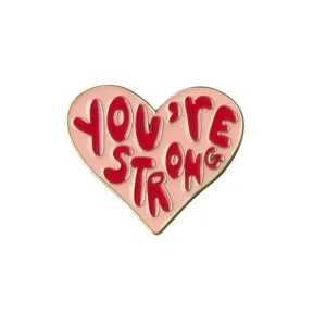 Close-up detail shot of a pink heart-shaped enamel brooch featuring bold red text.