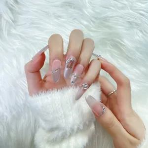 Primer plano de uñas postizas nude degradadas hechas a mano con finos bordes de pedrería plateada.