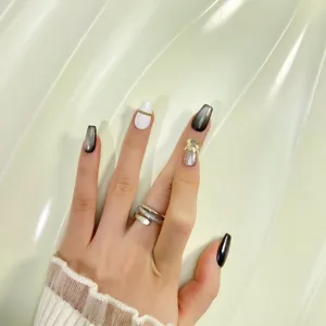 Vista detallada de uñas postizas hechas a mano con degradado blanco y negro y hoja de oro.