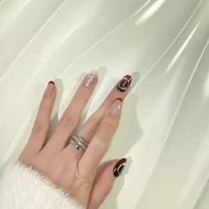 Faux ongles faits main en bordeaux avec effet cat-eye et détails de strass scintillants.