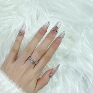 Detalle de uñas postizas con pedrería hechas a mano con borde de diamante plateado.
