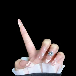 Gros plan d'ongles press-on nude rose faits main ornés de nœuds et de strass scintillants.