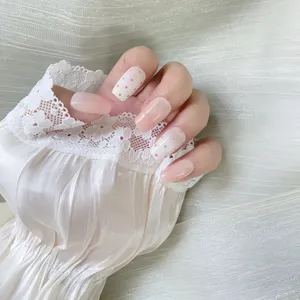 Close-up detail of nude pink press-on nails featuring cute polka dots and lace cuff.