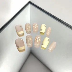 Handmade press-on nails detail, nude and yellow color block with glitter stars and rhinestones.