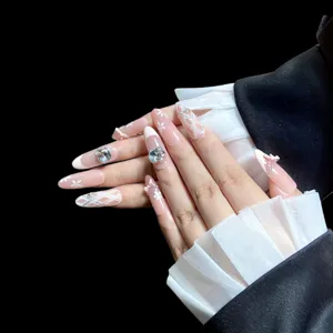 Faux ongles faits main rose nude longs avec strass brillants, jolis nœuds et fleurs délicates.