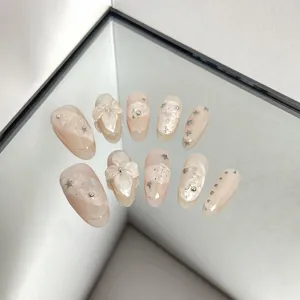 Close-up detail of nude pink press-on nails featuring 3D floral art and silver star rhinestones.