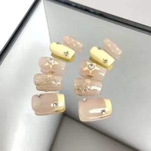 Detail view of handmade press-on nails, nude and yellow color block with rhinestones and stars.