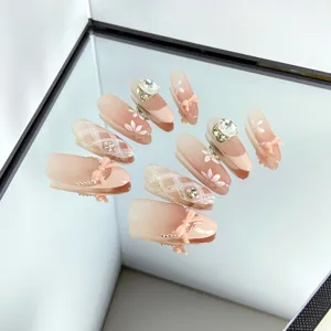 Faux ongles nude faits à la main avec strass scintillants et beaux nœuds pour un style élégant et chic.