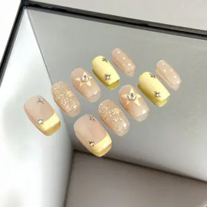 Close-up detail of handmade nude and yellow press-on nails featuring star and glitter decors.