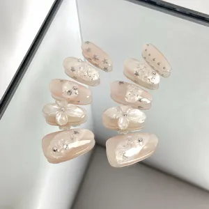 Close-up detail of nude pink press-on nails featuring 3D floral design and shimmering stars.