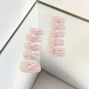 Primer plano de uñas postizas rosas hechas a mano con pedrería de corazón y perlas.
