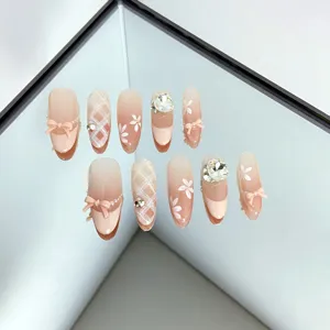 Ongles faits main nude rose détail avec jolis nœuds papillon et strass brillants.