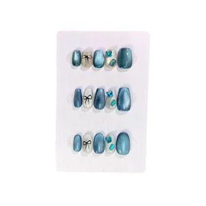 Uñas postizas ojo de gato azul con lazos negros y brillantes dijes de mariposa con pedrería fina.