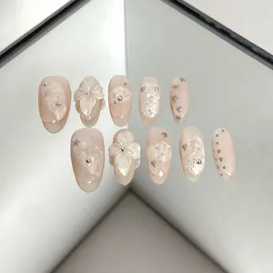 Detailed close-up of nude pink press on nails featuring 3D flowers and sparkling stars.