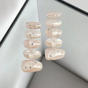 Delicate nude pink press-on nail details featuring sparkling stars, rhinestones, and 3D floral art.