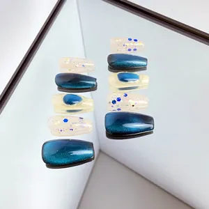 Faux ongles faits à la main avec effet œil-de-chat bleu et design scintillant.