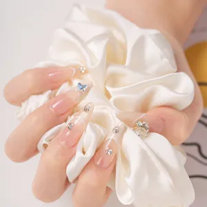 Faux ongles longs en amande luxueux avec strass en coeur et chouchou en satin doux.