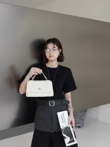 Détail rapproché d'un sac carré blanc chic à poignée tenu par un mannequin, élégant.