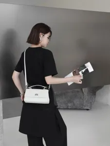 Vue détaillée du sac bandoulière en cuir blanc avec fermoir métallique et poignée portée.