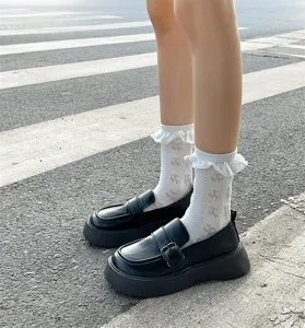 Close-up of white frilly lace mid-tube socks paired with black platform loafers on street.