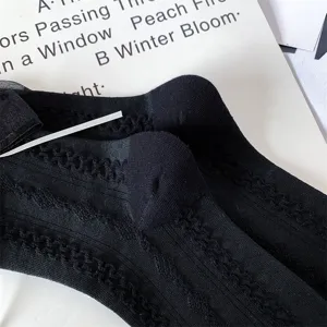 Close-up of Japanese style black mid-calf socks featuring delicate lace texture and side bow.