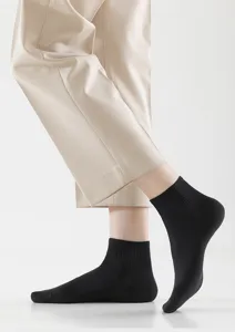 Nahaufnahme von atmungsaktiven schwarzen Sneakersocken mit hellen Hosen vor klarem Hintergrund.