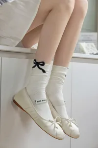 Calze bianche al polpaccio con fiocco nero e scarpe basse da ballerina abbinate per la primavera.