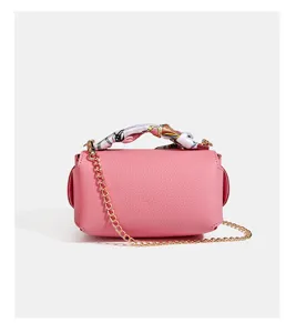 Close-up of pink leather box bag detail with gold chain strap and stylish silk scarf handle.